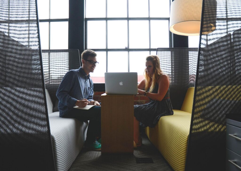 Duas pessoas sentadas num ambiente de trabalho, usando um computador